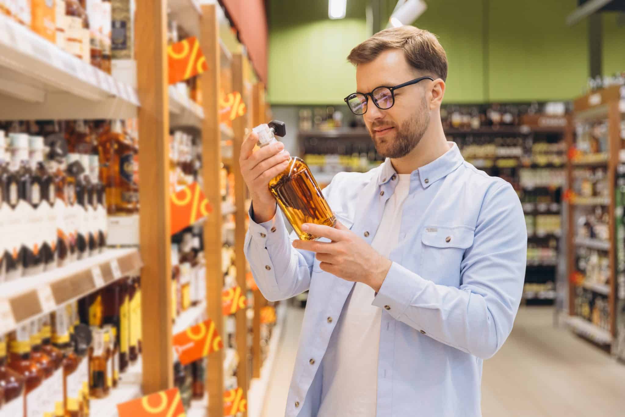 Customer Choosing Alcoholic Beverage in Supermarket Alcohol Section Man reading label of whiskey bottle, shopping in liquor store, choosing alcohol